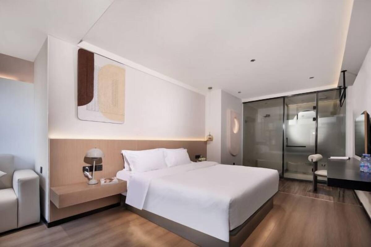 Ein modernes Hotelzimmer mit einem großen Bett, Nachttischen, einem Schreibtisch und einer Duschkabine aus Glas.