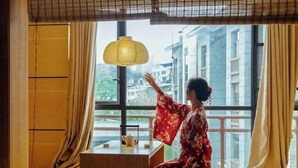 Een kamer met een traditioneel Japans design, met tatami vloeren, een lage houten tafel met een theepot en een groot raam met gordijnen.