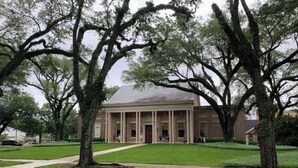 A building with a central portico and columns, surrounded by trees and a well-maintained lawn.