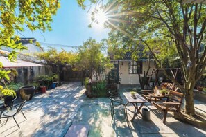 An outdoor patio area with tables and chairs, surrounded by potted plants and trees.