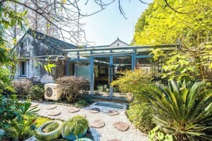 Um jardim com uma estrutura de vidro, um edifício com telhado em telhas e diversas plantas.