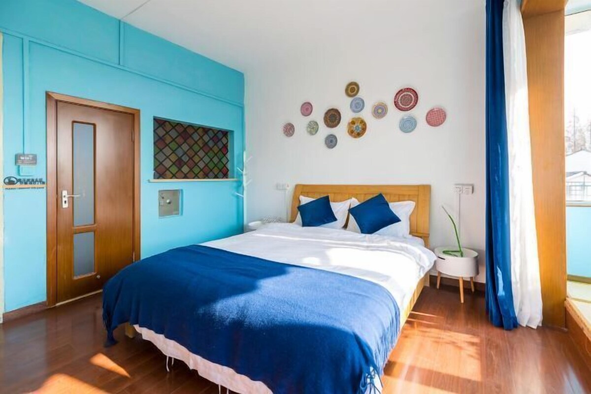 Quarto com cama, porta de madeira, janela com persianas e parede com detalhes circulares.