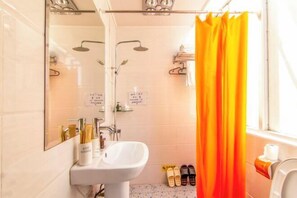 Casa de banho com lavatório branco, espelho, chuveiro com porta de vidro e cortina amarela.
