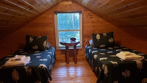 Un dormitorio acogedor en el ático con dos camas, una mesita y una ventana con vistas a árboles.