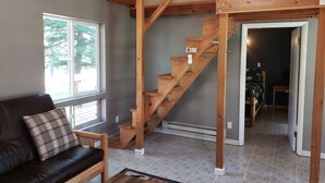 Una habitación con escalera de madera, sofá de cuero y vistas al exterior por una ventana.