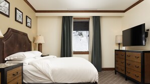 A hotel room with a large bed, a dresser, a television, and a window with curtains.