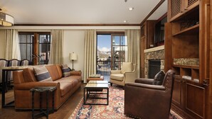 A cozy living room with a sofa, armchair, and coffee table, a fireplace, and a view of mountains through large windows.