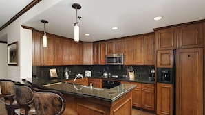 A kitchen with wooden cabinets, a granite countertop, stainless steel appliances, and bar stools.
