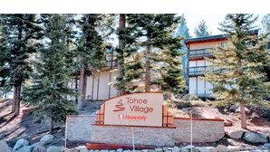 A sign for Tahoe Village with a view of a building and trees.