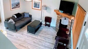A modern living room with a grey sofa, a coffee table, a TV on a wooden stand, and framed pictures on the wall.