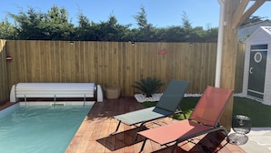 Een houten terras met een zwembad, twee ligstoelen, een bankje en een kleine tuinhuis.
