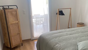 Een slaapkamer met een bed, houten vloer, een kledingkast en een deur naar een balkon.