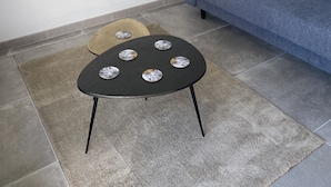 Een woonkamer met een blauwe bank, een klein zwart tafeltje met decoratieve borden, een grijze vloerkleed en een schilderij van een ruig landschap aan de muur.