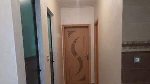 Ein schmaler Flur mit einer Holztür, die ein Halbmonddesign zeigt, einem kleinen Teppich auf dem Boden und einer Deckenleuchte.