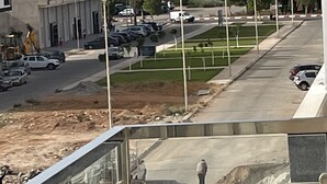 Blick vom Balkon auf eine Baustelle mit Straße, parkenden Autos und einem Gebäude mit Balkonen.