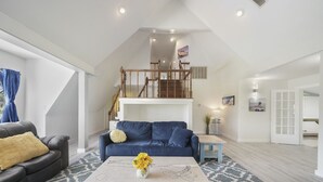 En rummelig opholdsstue med højt til loftet, en blå sofa, et hvidt sofabord med blomster og en trappe til øvre plan.