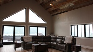 A spacious living room with a large sectional sofa, a wooden coffee table, and a ceiling fan. There are large windows offering views of the outdoors. - High tech modern farmhouse in Franklin, NY (Franklin)