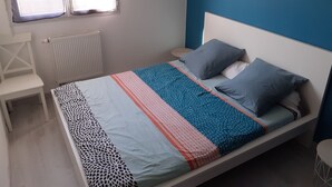 A neatly arranged bedroom with a bed, a small bedside table, a chair, and a window.