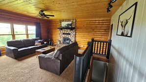 A log cabin interior with a fireplace, two sofas, a coffee table, and a dining table.