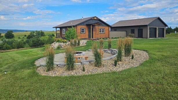A log cabin with a stone fire pit surrounded by a landscaped garden.