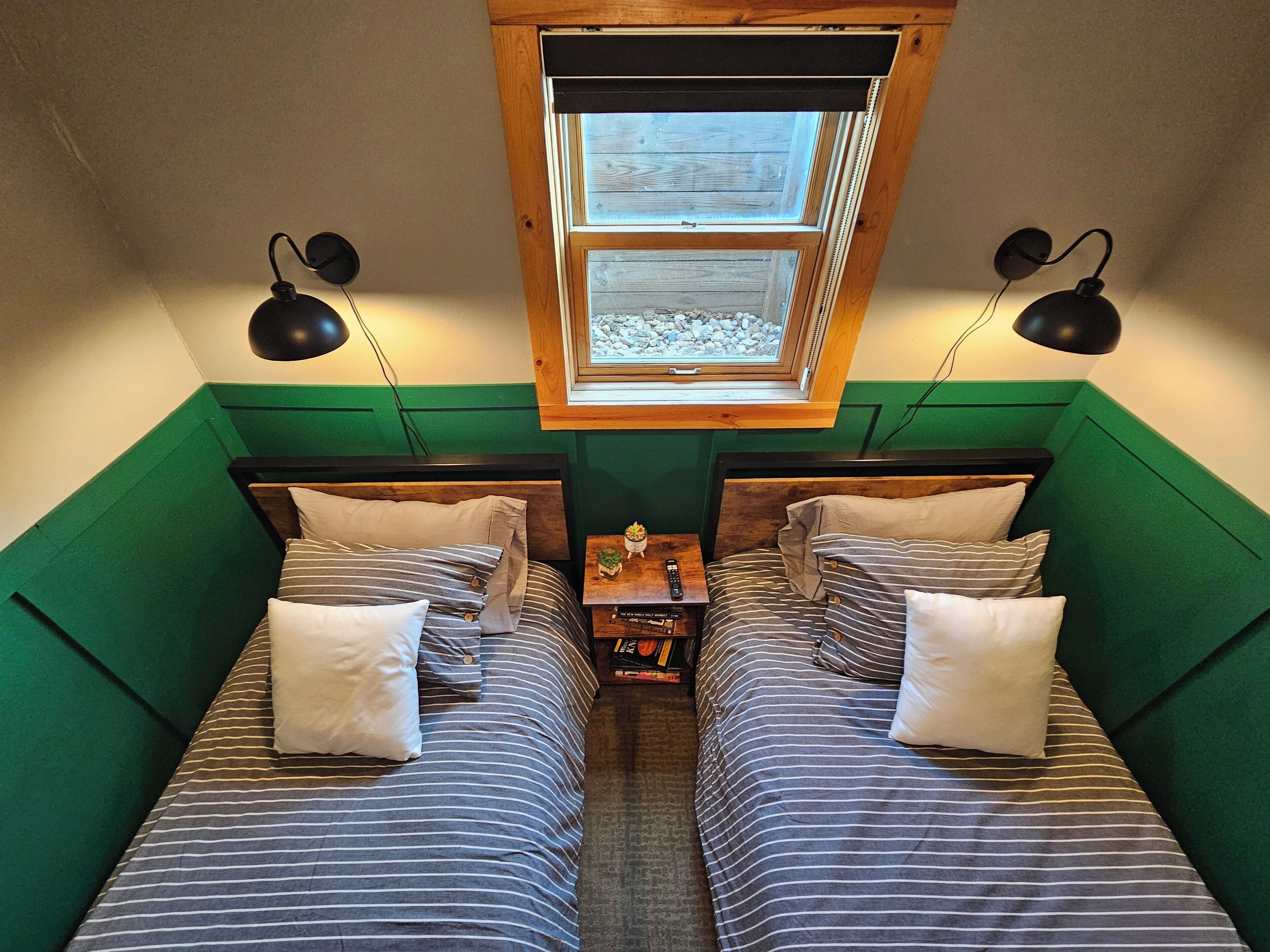 A small, cozy room with two single beds, green walls, a skylight, and two wall-mounted lamps.