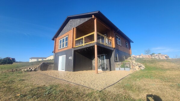 A two-story log cabin with a balcony, a covered porch, and a stone retaining wall.