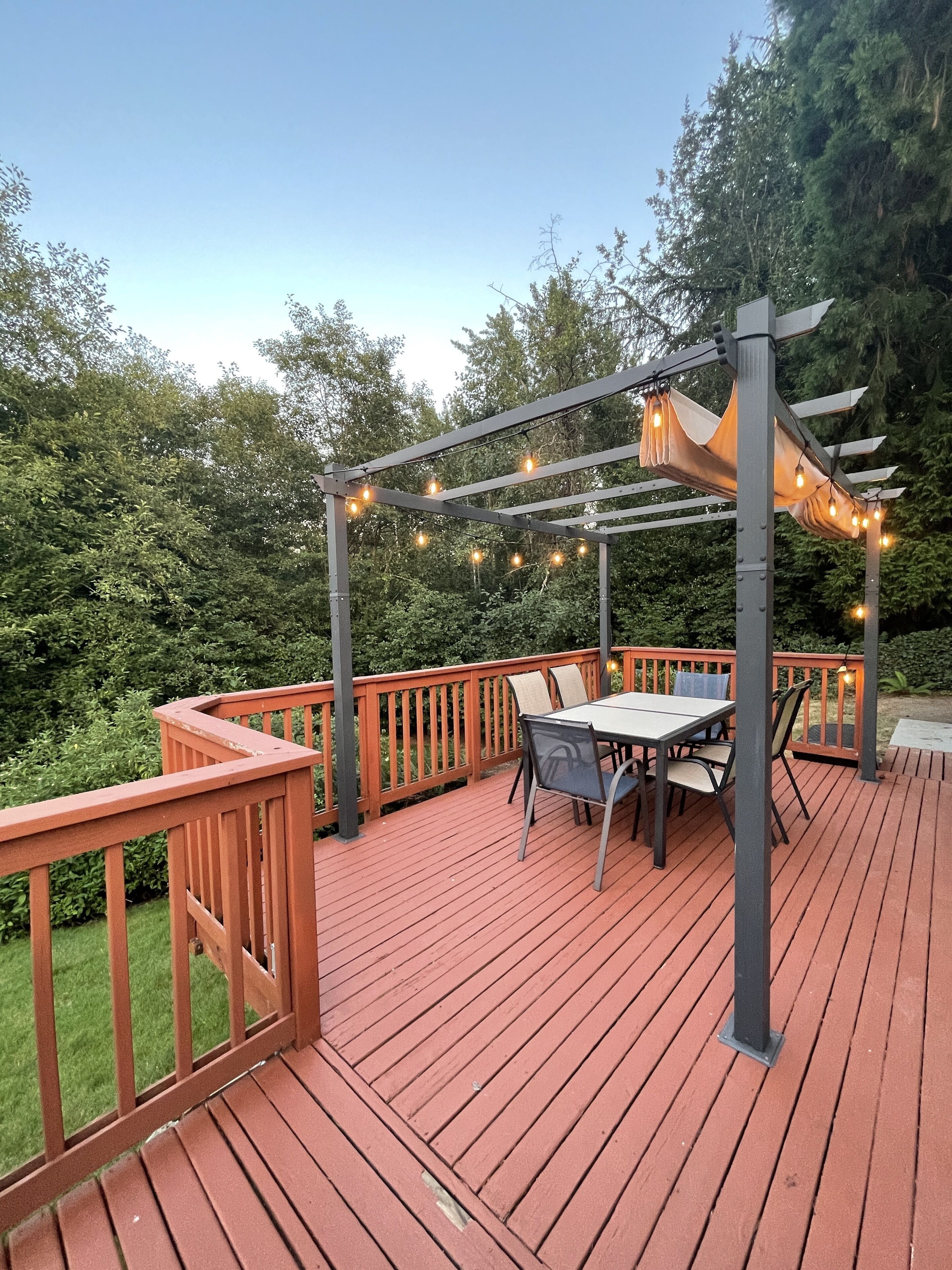 A wooden deck with a table and chairs, surrounded by a wooden railing and string lights.
