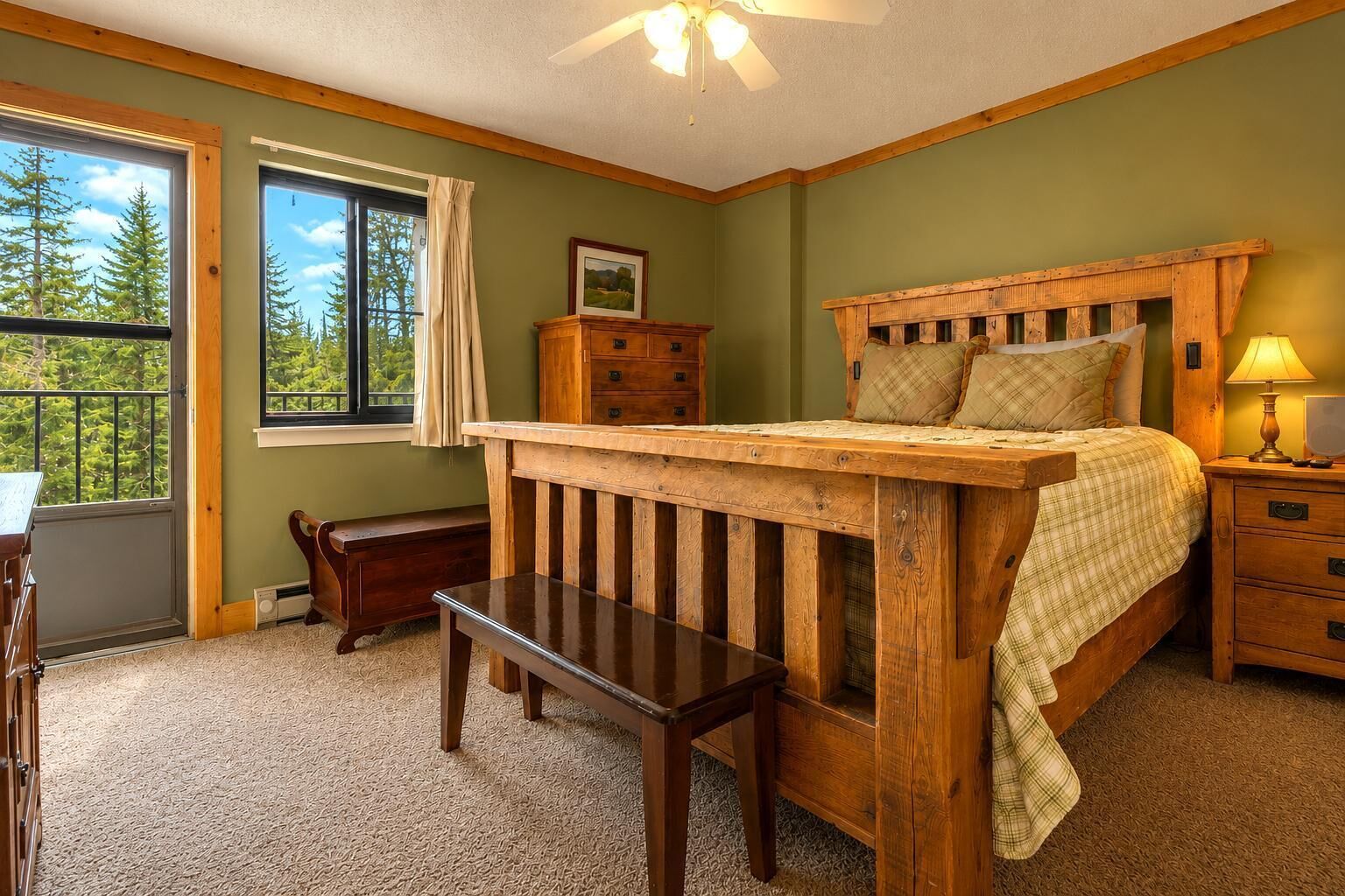 Une chambre à coucher avec un lit en bois, un banc, une commode et une fenêtre donnant sur des arbres.