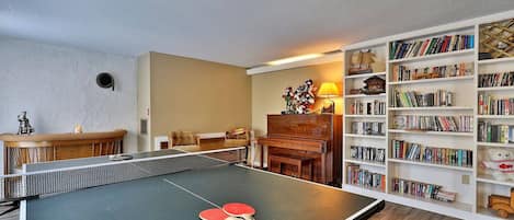 A room with a ping pong table, a piano, a bookshelf, and a sofa.