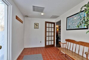 A hallway with a tiled floor, a wooden bench, a door with a glass panel, a wall-mounted sign, and a framed map. - Charming multi-level 3 Bedroom home 15 minutes from Killington Mountain (Killington)