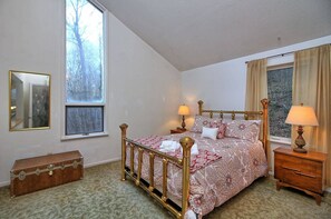 A bedroom with a four-poster bed, two bedside tables, a wooden chest, and a large window with curtains.