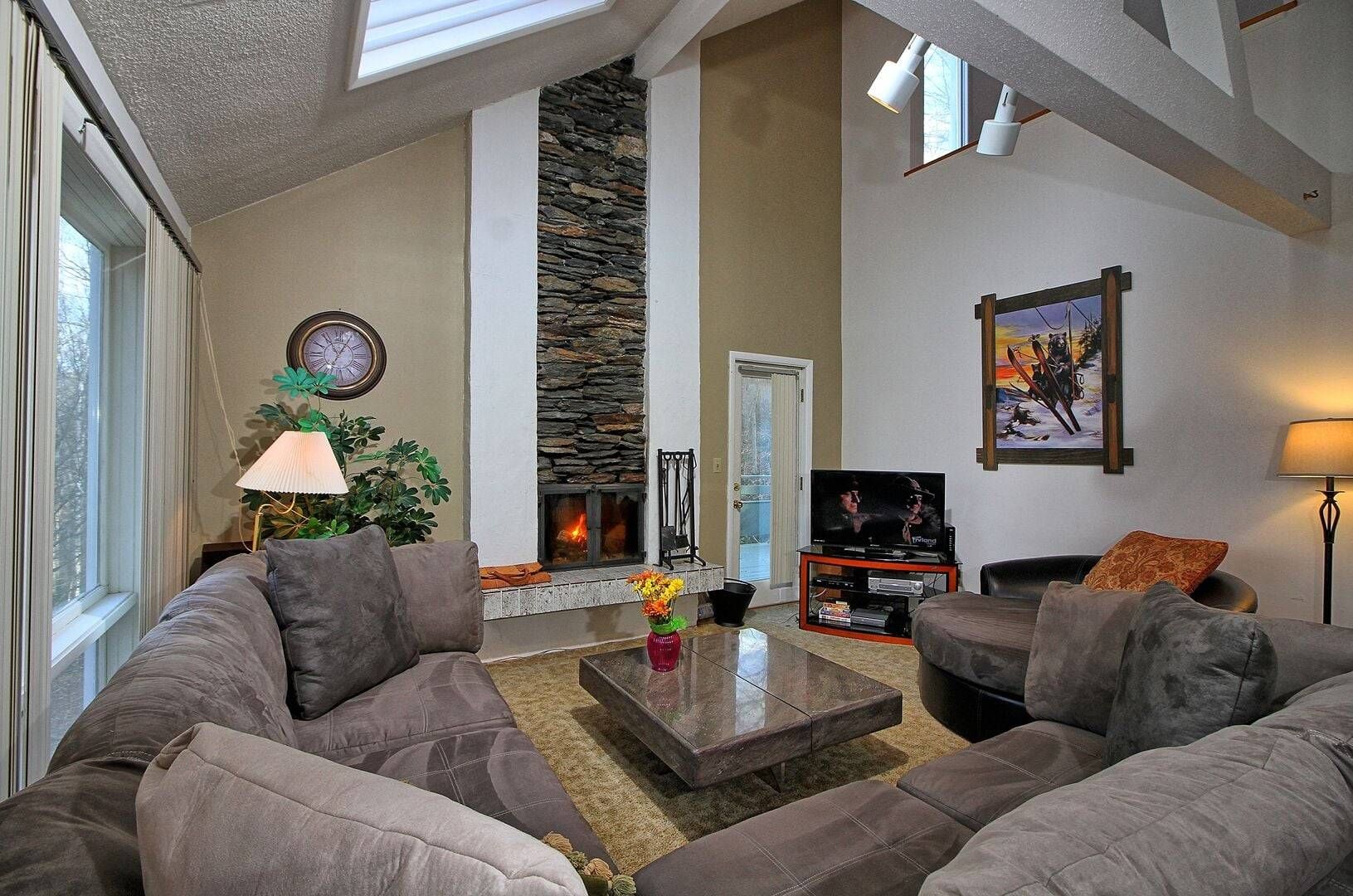 A living room with a stone fireplace, a television, and a large window.