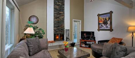 A living room with a stone fireplace, a television, and a large window.