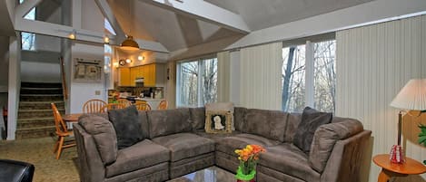 A modern living room with a sectional sofa, a coffee table, and a dining area with wooden chairs.