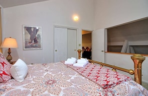 Een hotelkamer met een bed, een bedlamp, een spiegel en een lijst met een afbeelding aan de muur.