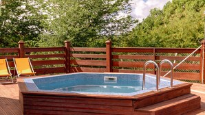 Une terrasse en bois avec un jacuzzi, entourée d’une clôture en bois et agrémentée de chaises orange.