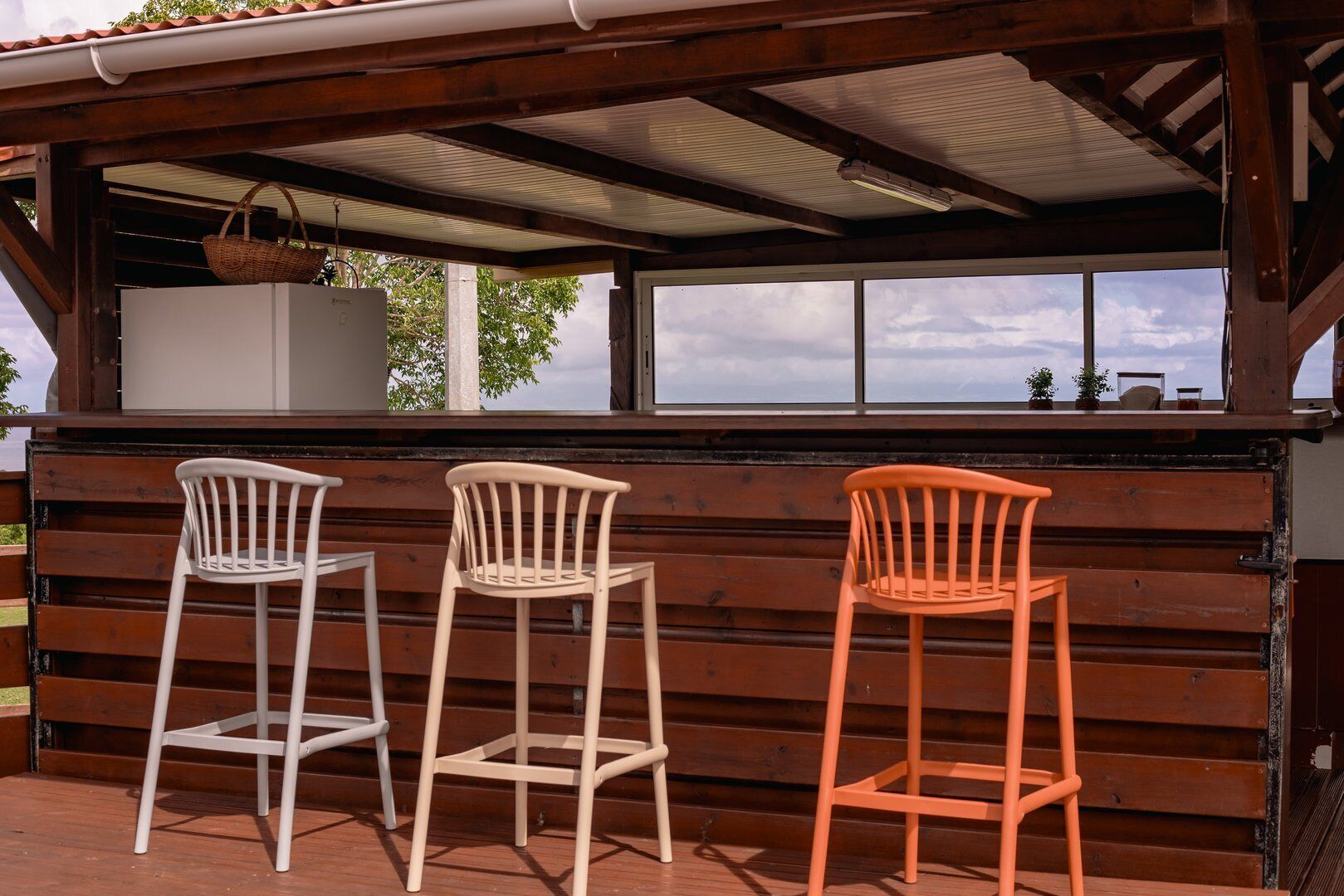 A wooden bar area with three chairs, a white cabinet, and a view of the outdoors.