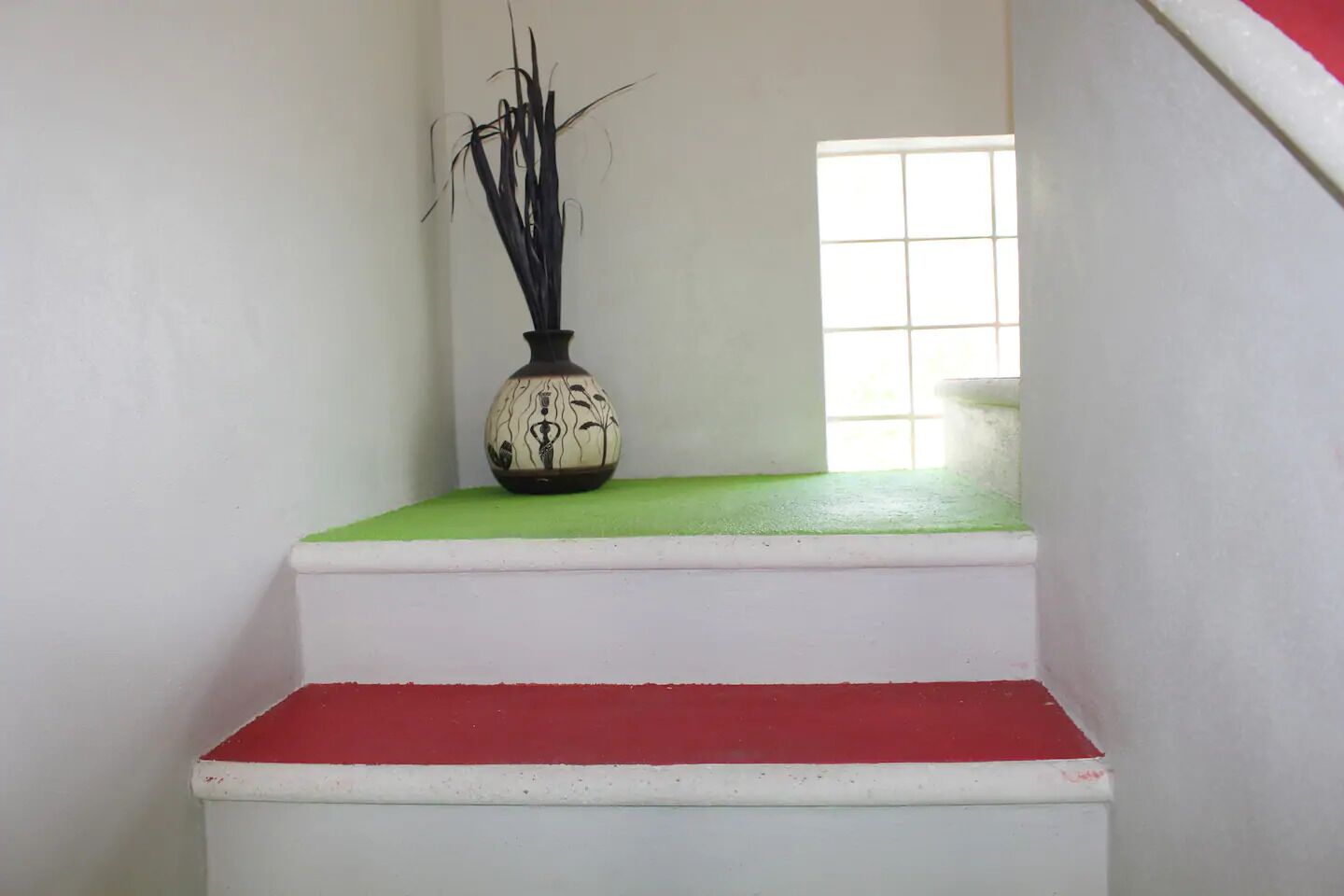 A staircase with a vase of black and white flowers on a green ledge.