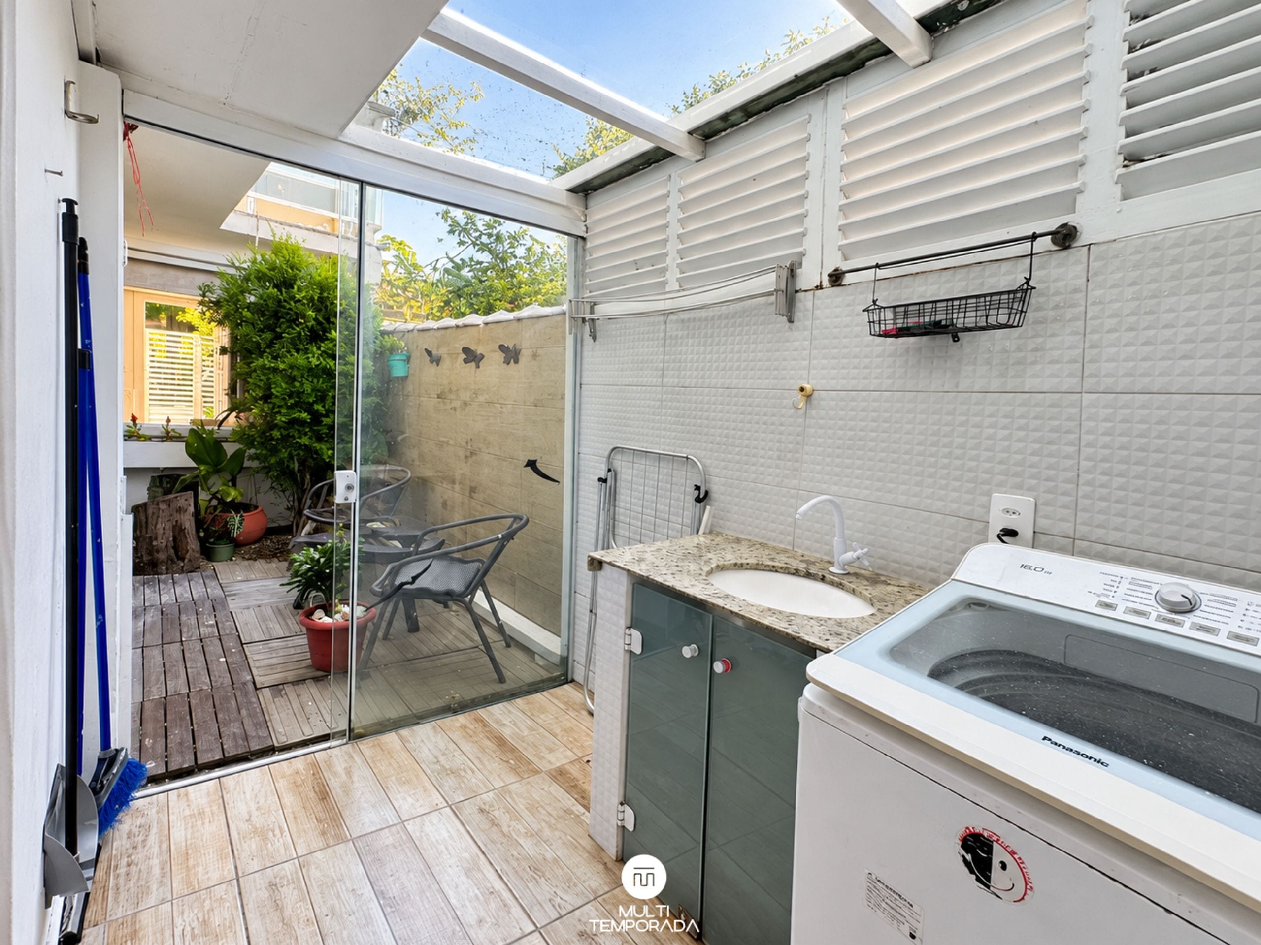 Un baño moderno con una puerta de vidrio que da a un patio, lavadora integrada y un lavamanos pequeño.