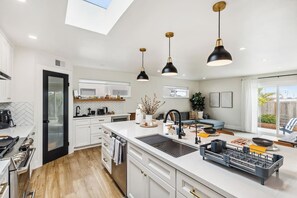 A modern kitchen with a central island, pendant lighting, and a view to the backyard. - LuxoStays | ! Modern 3B #KING bed #SFO#Family (South San Francisco)