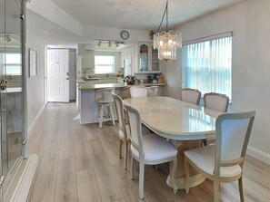 Una cocina moderna con una isla central, armarios blancos y un comedor con una mesa de mármol y sillas blancas.