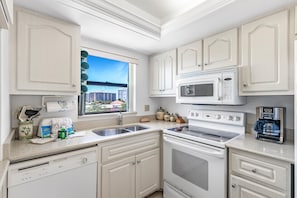 A modern kitchen with white cabinetry, a built-in microwave, an oven, and a coffee maker. - Estero Cove 341 (Fort Myers Beach)