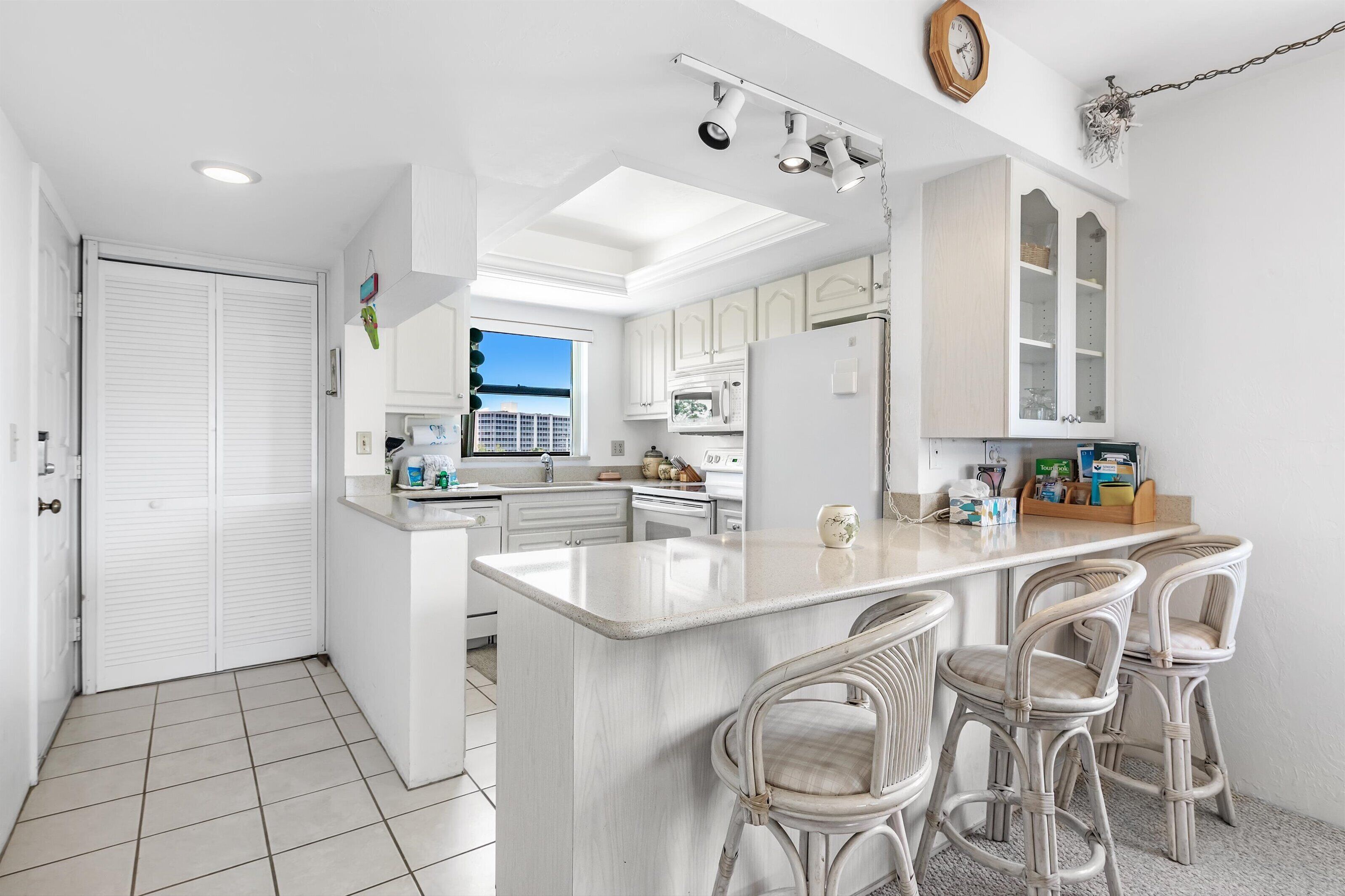 A modern kitchen with white cabinetry, a large island with bar stools, and a view of the city through the window.