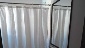 Un baño con cortina de ducha, lavamanos, espejo y toallero.