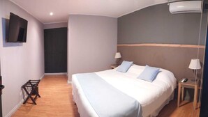 Habitación de hotel con una cama grande, un televisor montado en la pared, piso de madera y una puerta con el número 14.
