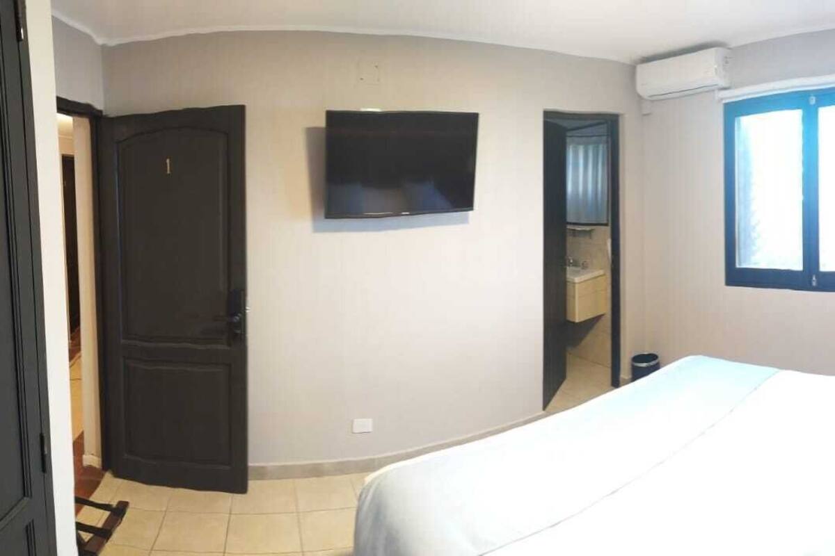 Ein Schlafzimmer mit einem Bett, einem an der Wand montierten Fernseher, einem Fenster und einer Tür.