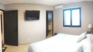 Un dormitorio con una cama, un televisor en la pared, una ventana y una puerta.
