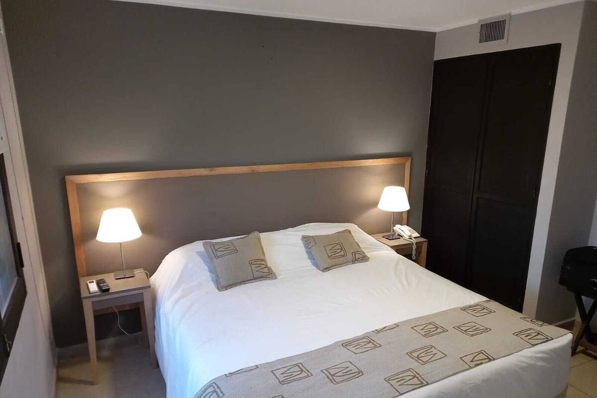 Ein Hotelzimmer mit einem großen Bett, zwei Nachttischlampen, einem Nachttisch mit Telefon und einer geschlossenen Tür.