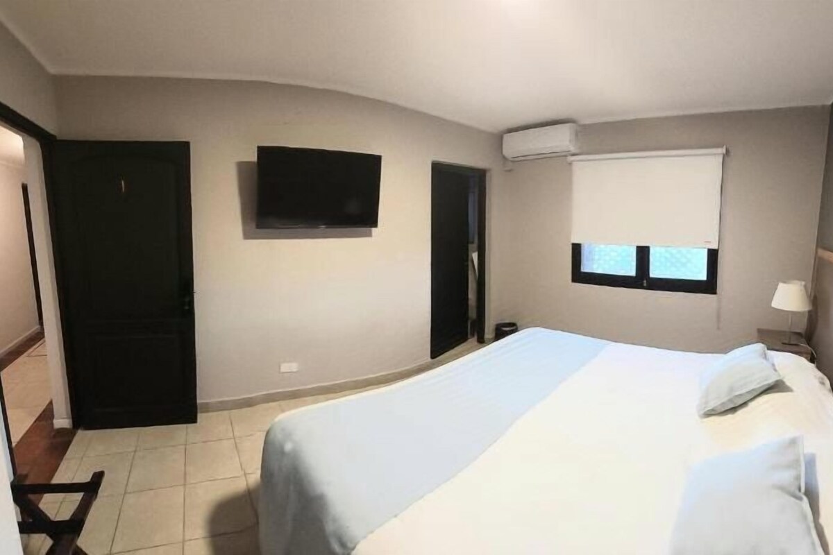 Una habitación de hotel con una cama, un televisor, una ventana con persianas y una puerta.