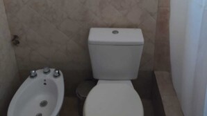 Un baño con inodoro, bidé y paredes de azulejos.